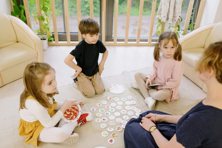 adulte discutant avec 3 enfants autour d'un jeu au sol