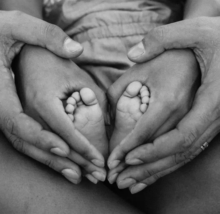 Mains des parents entourant les pieds de bébé en formant des coeurs