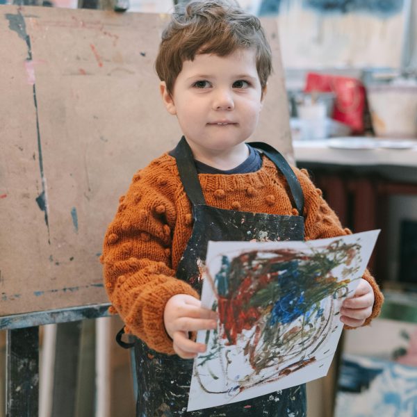 Petit garçon avec un tablier, montre son dessin de peinture