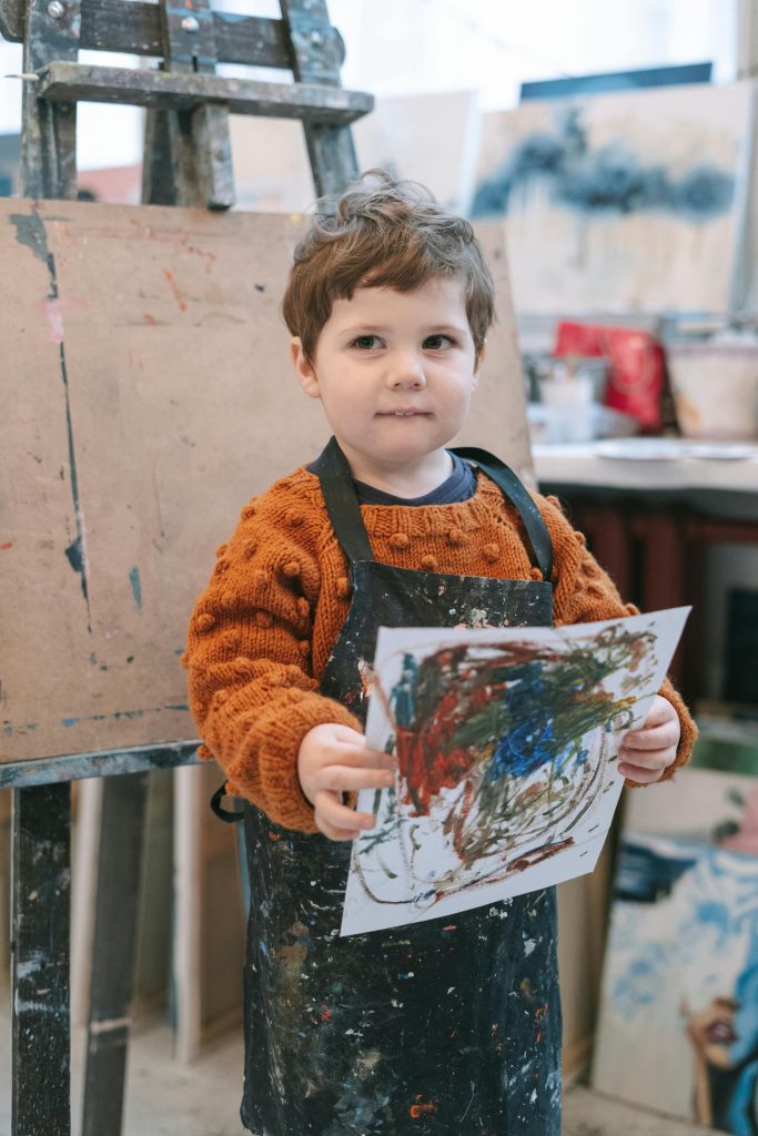 Petit garçon avec un tablier, montre son dessin de peinture