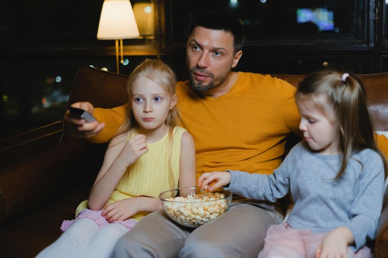 Un pére ayant un bol de pop corn sur ses genoux avec ses fille